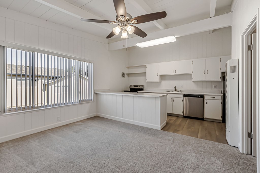 A white kitchen with a ceiling fan and a window with blinds.