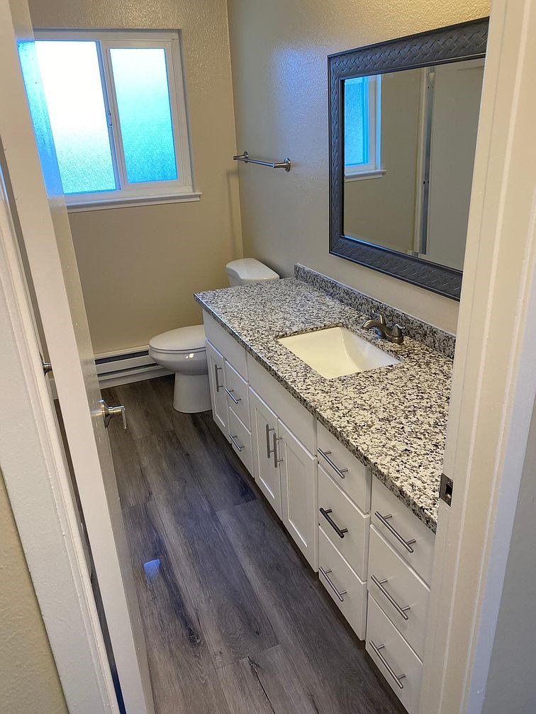 A bathroom with a granite counter top and white cabinets.