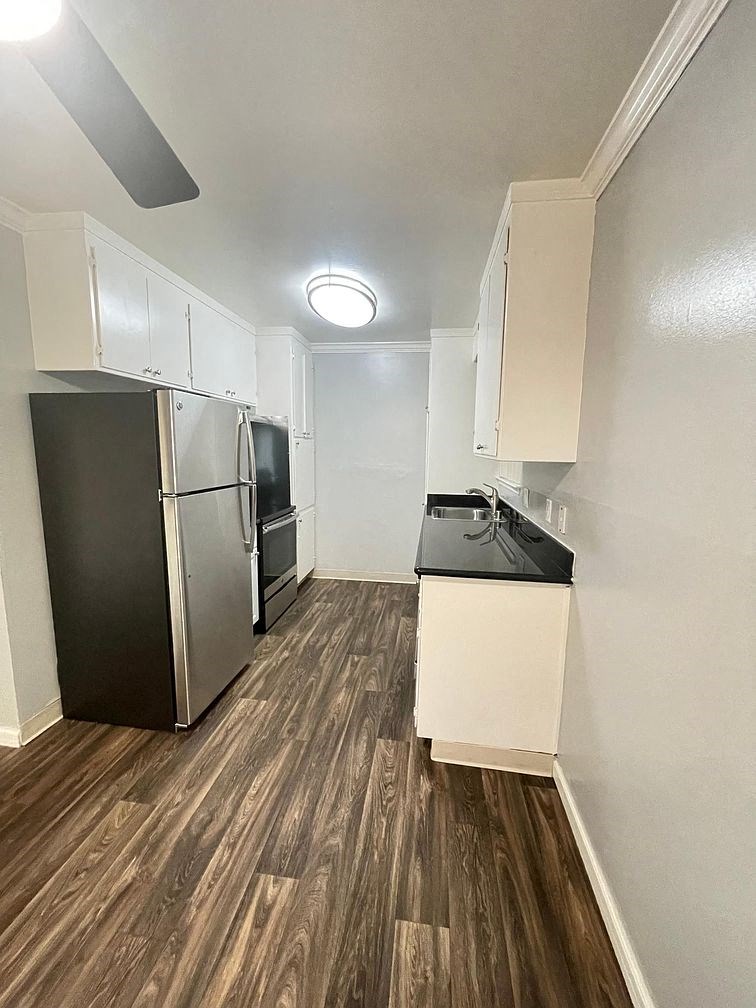 A kitchen with a black refrigerator and wooden floors.