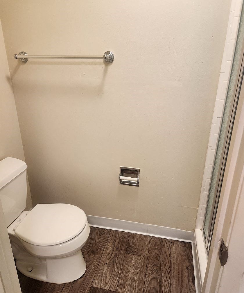 A white toilet in a small bathroom with wood flooring.