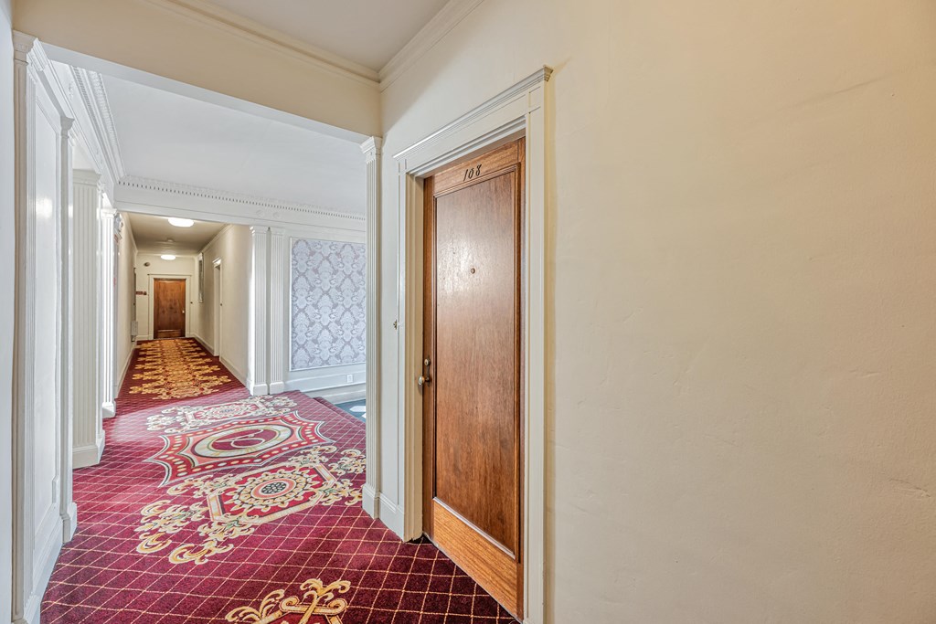 A hallway with a red carpet and a wooden door.