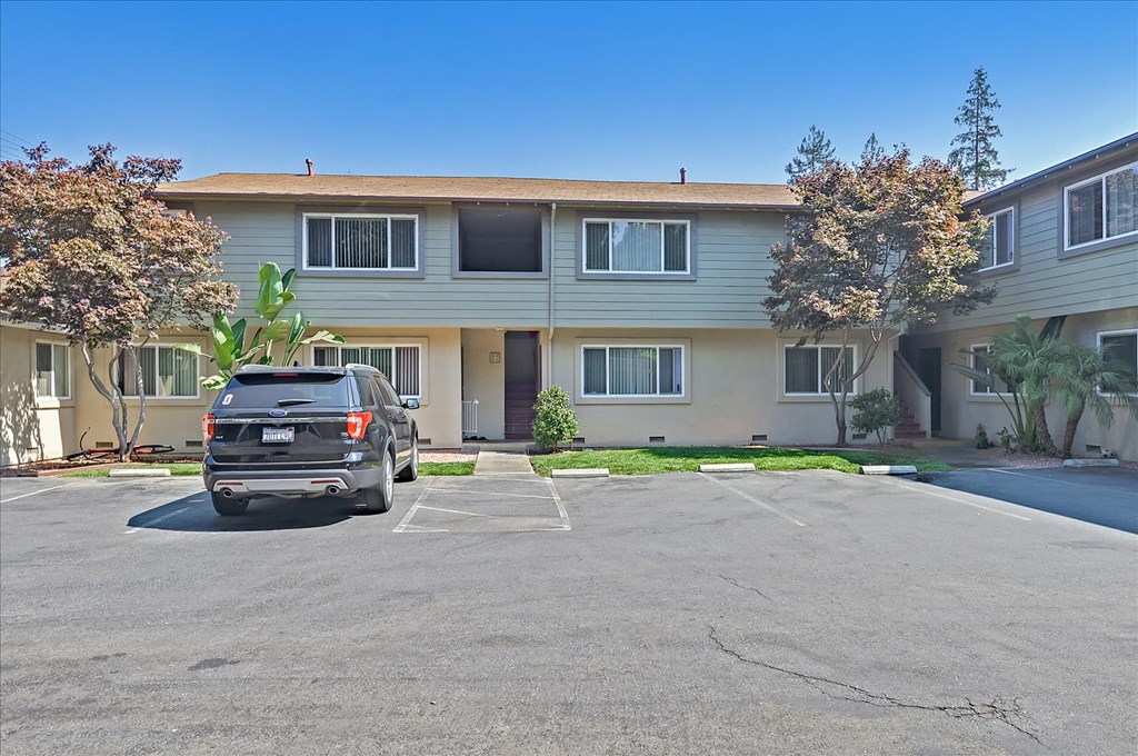 A black car is parked in a parking lot in front of a building.