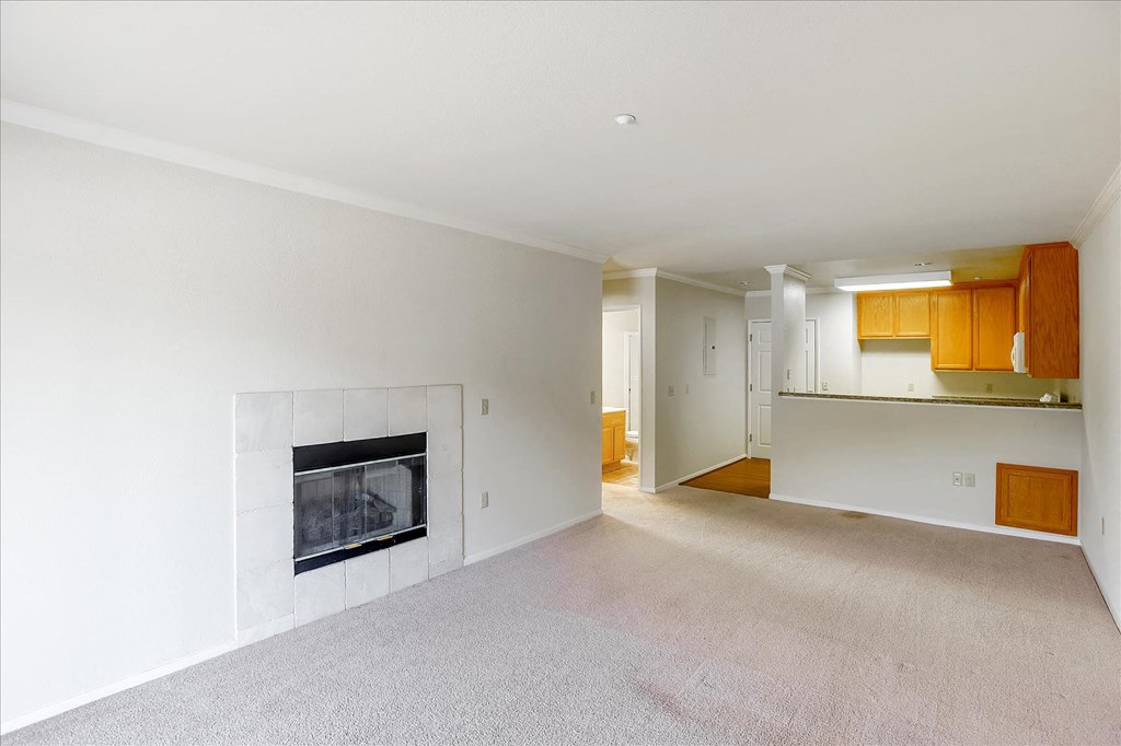 A large, empty living room with a fireplace and a kitchen in the background.