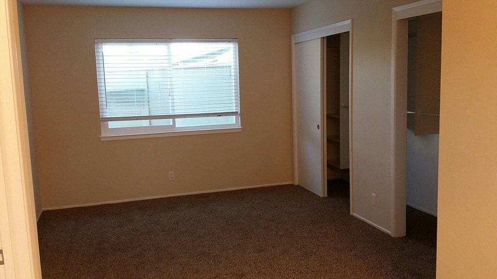 A room with a carpeted floor and a window with blinds.