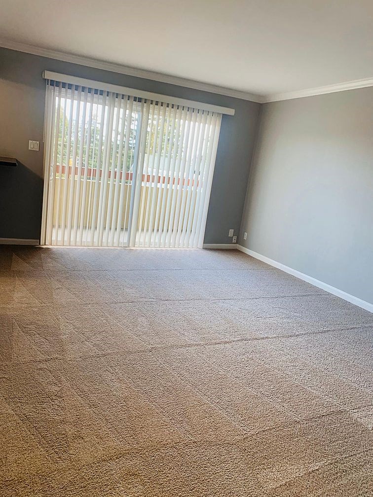 A room with a carpeted floor and a window with blinds.