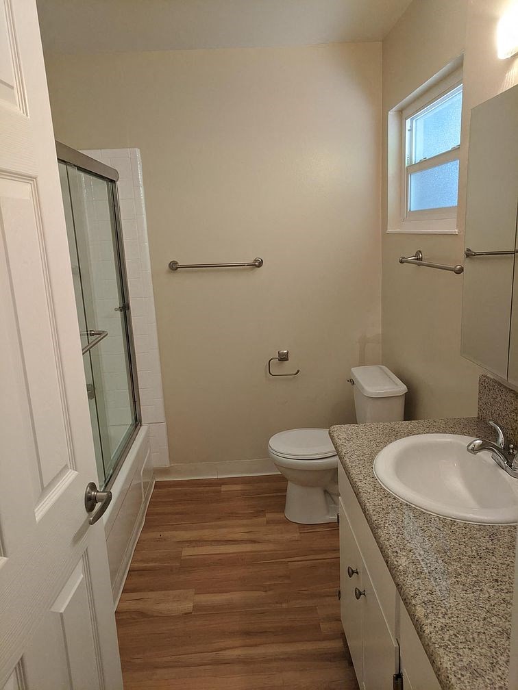 A white bathroom with wood floors and a window.