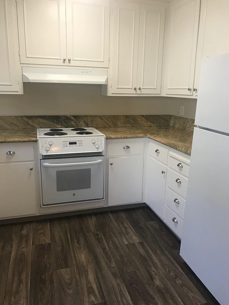 A white stove and refrigerator in a kitchen with wooden floors and white cabinets.