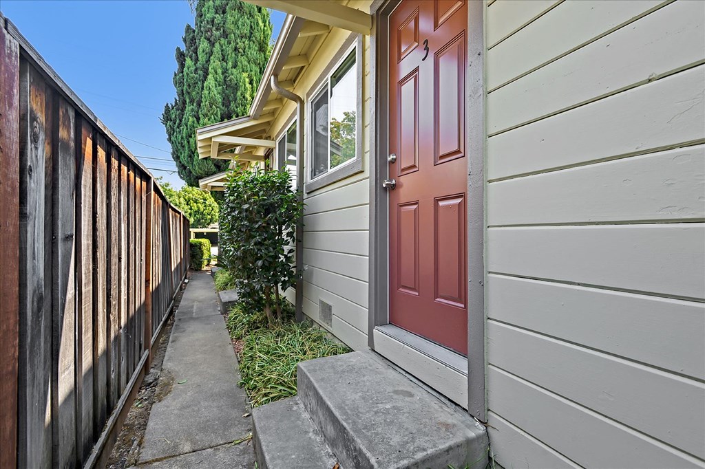 A red door is on the right side of a grey house.