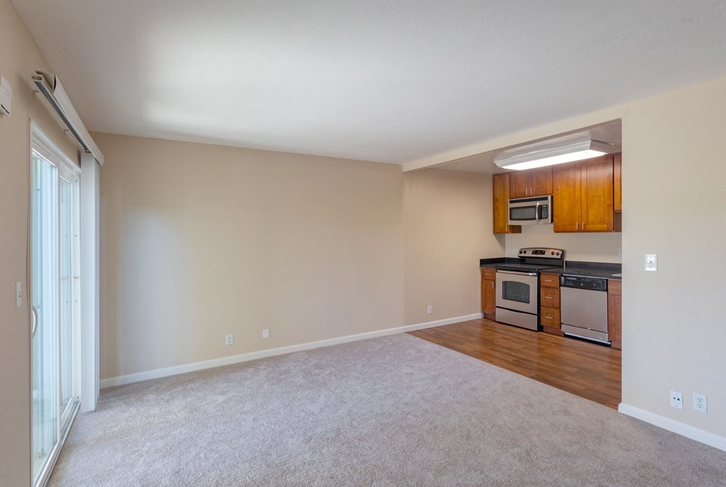 an empty living room and kitchen with wood cabinets and white carpet