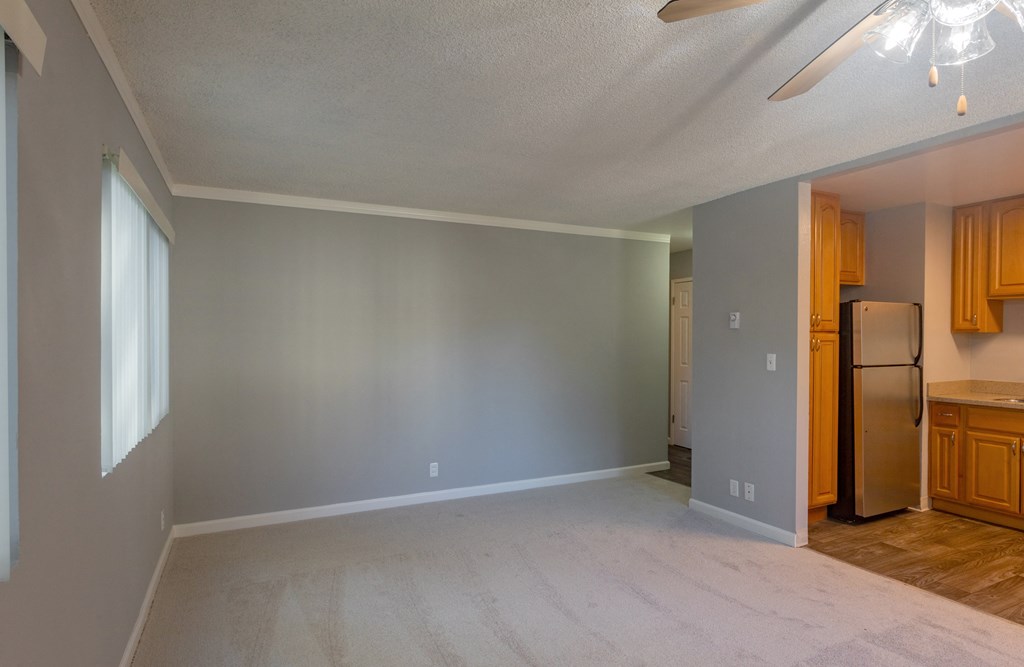 an empty living room with a refrigerator and a kitchen