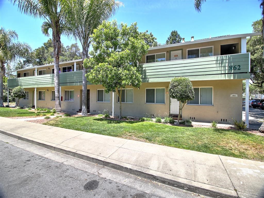 an apartment building with a sidewalk and trees in front of it