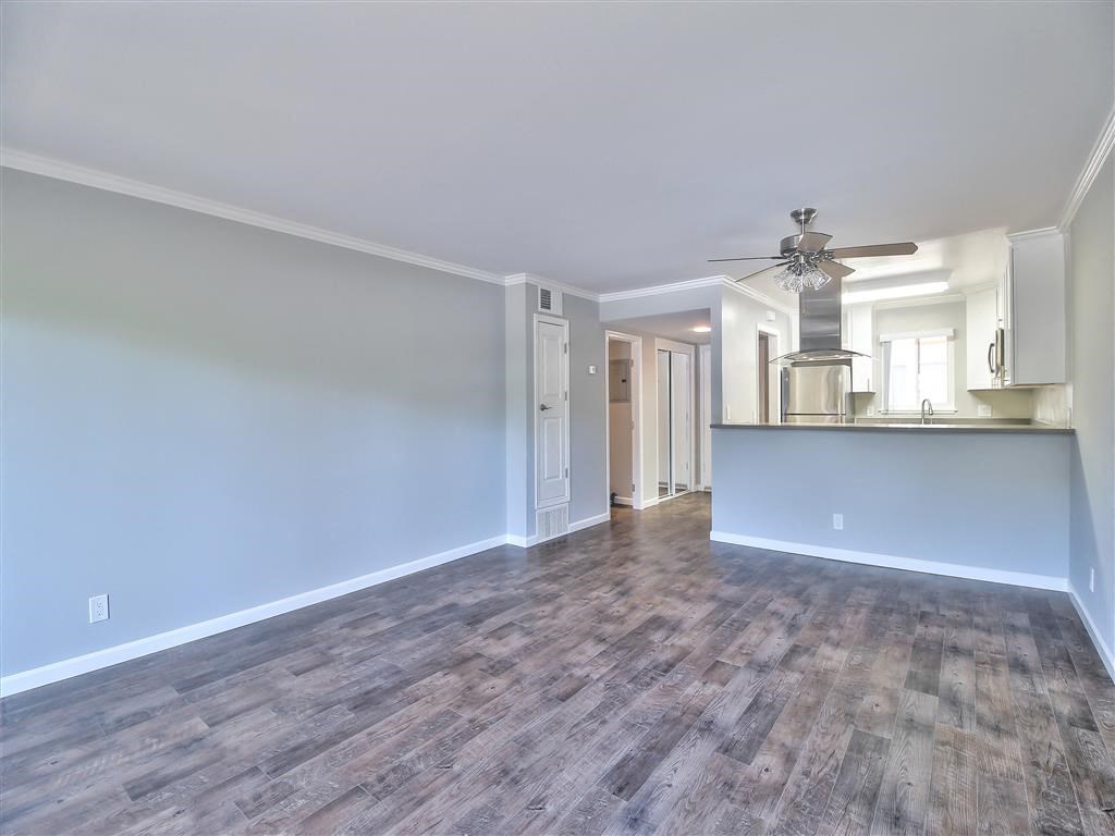an empty living room with a kitchen and a ceiling fan