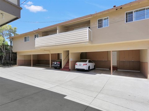 A white car is parked in a garage of a two-story apartment building.