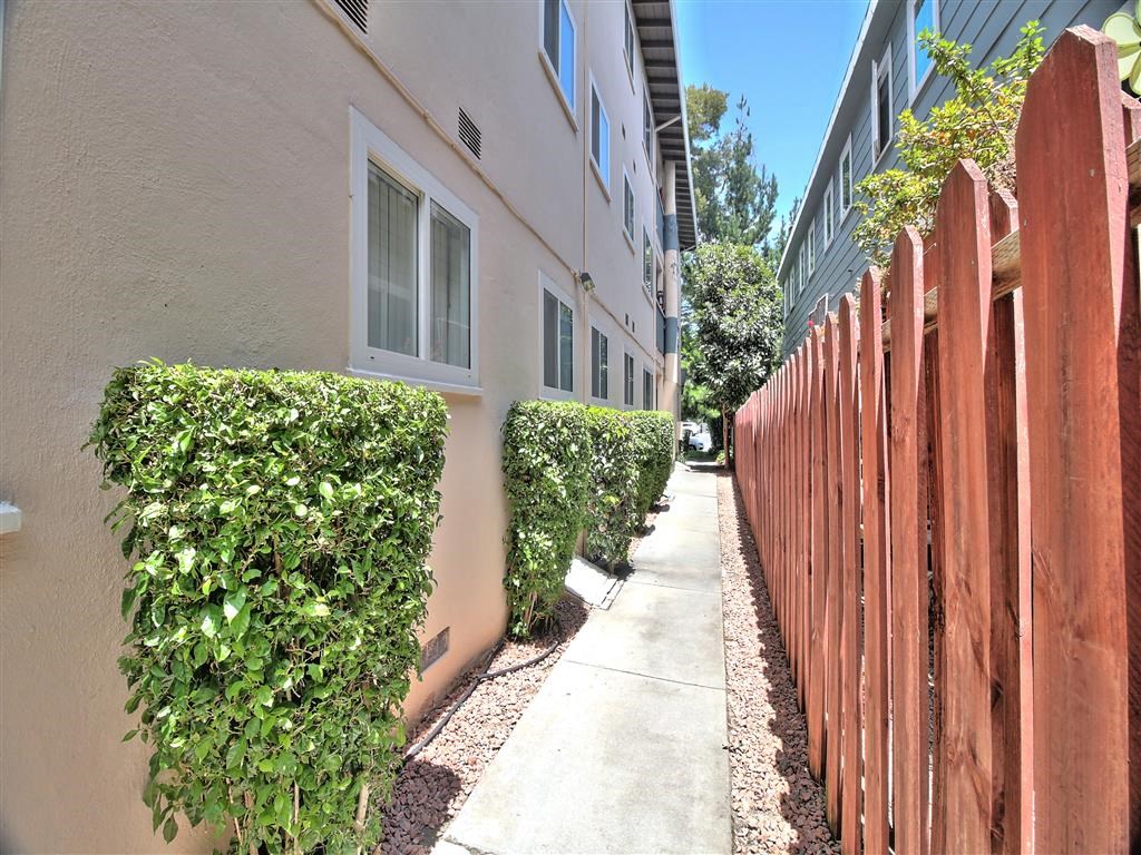 a sidewalk in front of an apartment building with a wooden fence