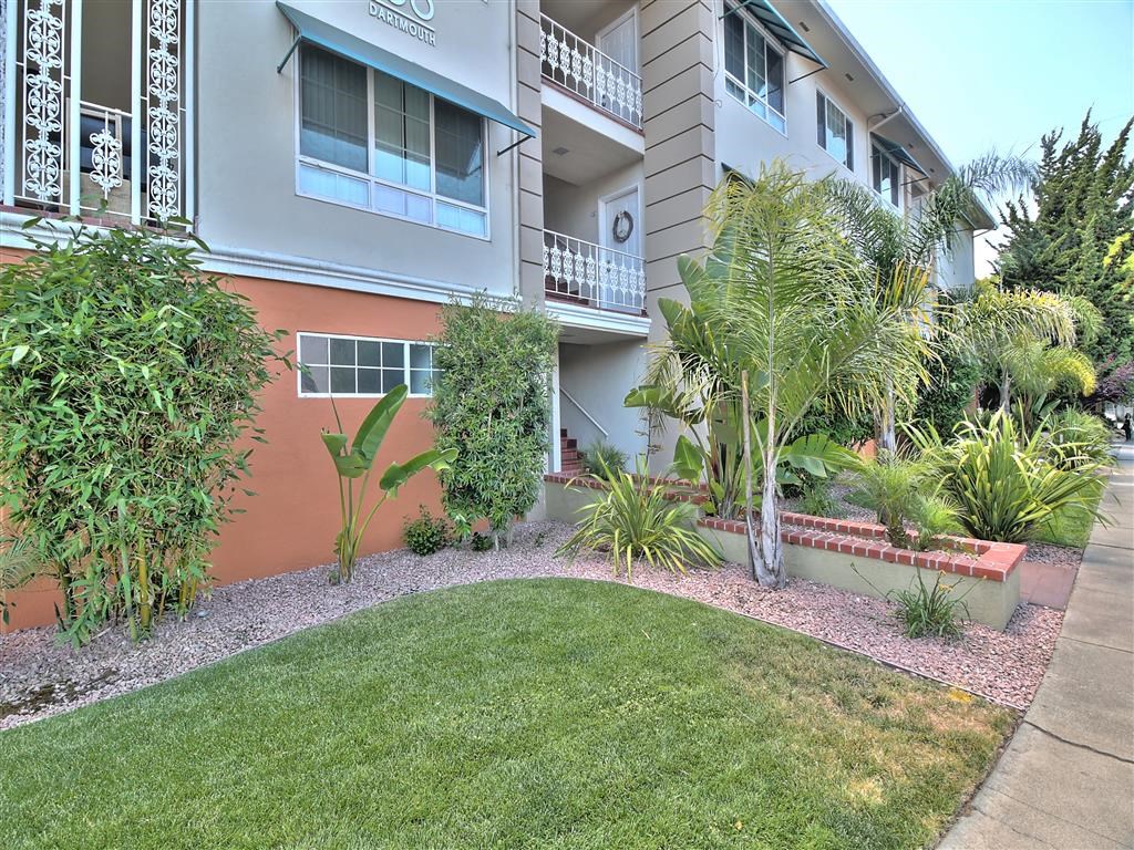 an apartment building with a lawn and plants in front of it