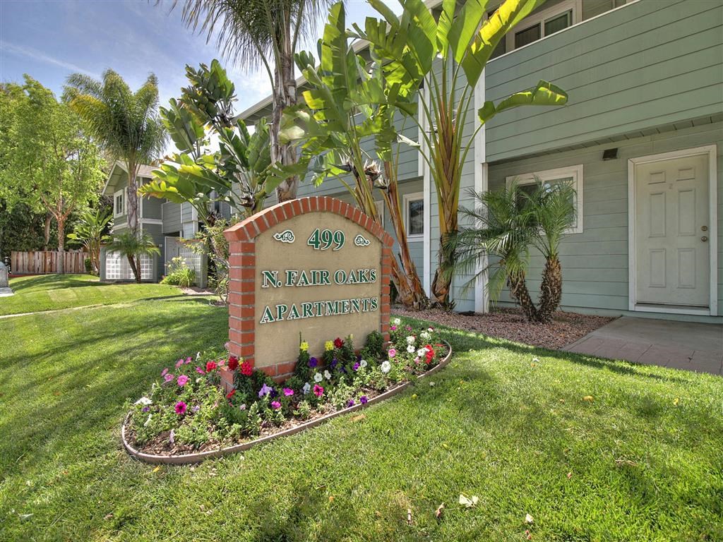 A sign for N. Fair Oaks Apartments is surrounded by flowers and greenery.