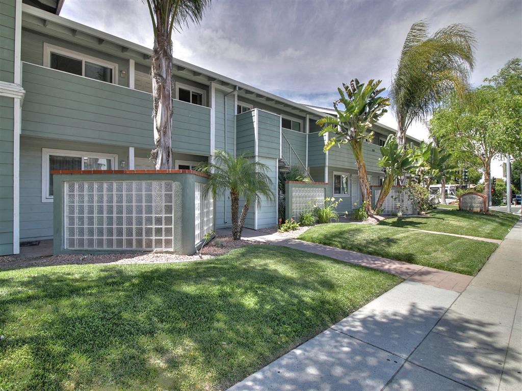 A row of green apartment buildings with a white fence and a tree in front.