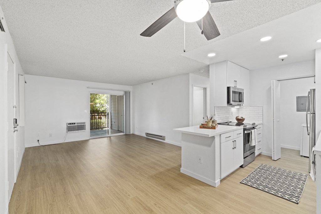 the living room and kitchen of a house with white walls and wood floors