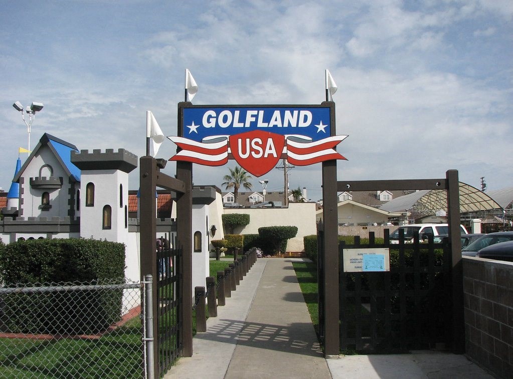 A sign that says Golfland USA is in front of a fence.