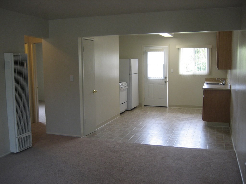A room with a carpeted floor and a white refrigerator.