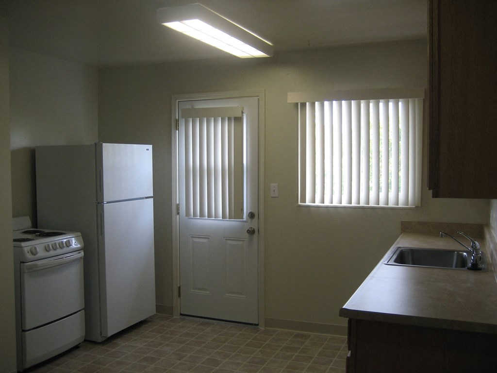 A kitchen with a white refrigerator, a white stove, and a white door.