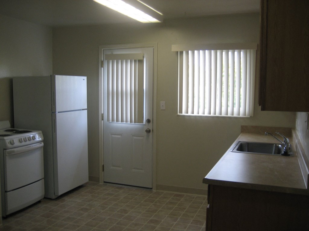 A kitchen with a white refrigerator, a white oven, and a white door.