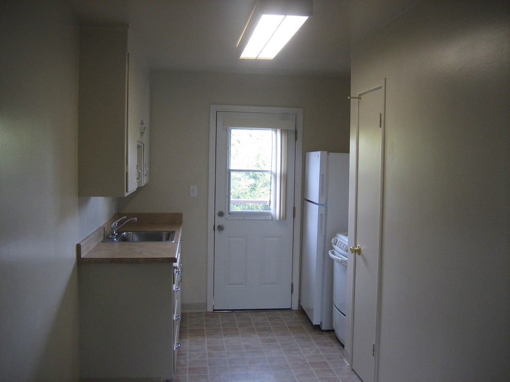 A kitchen with a sink, refrigerator, and a door leading to a patio.