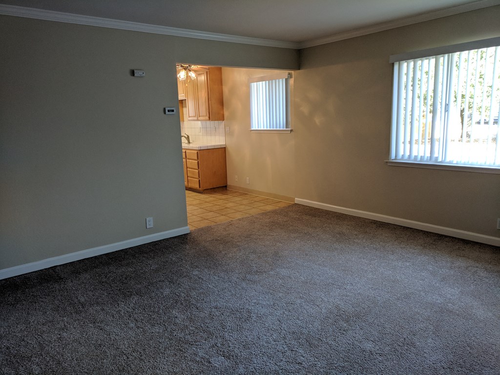 an empty living room with a kitchen in the background