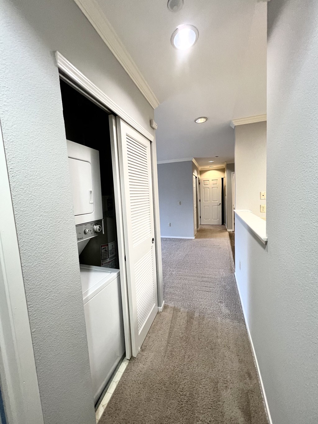 A narrow hallway with a white door on the left and a carpeted floor.