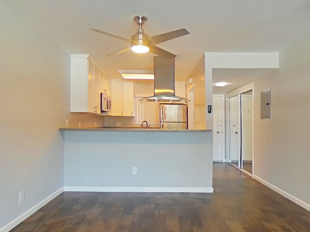 an empty living room with a kitchen and a ceiling fan