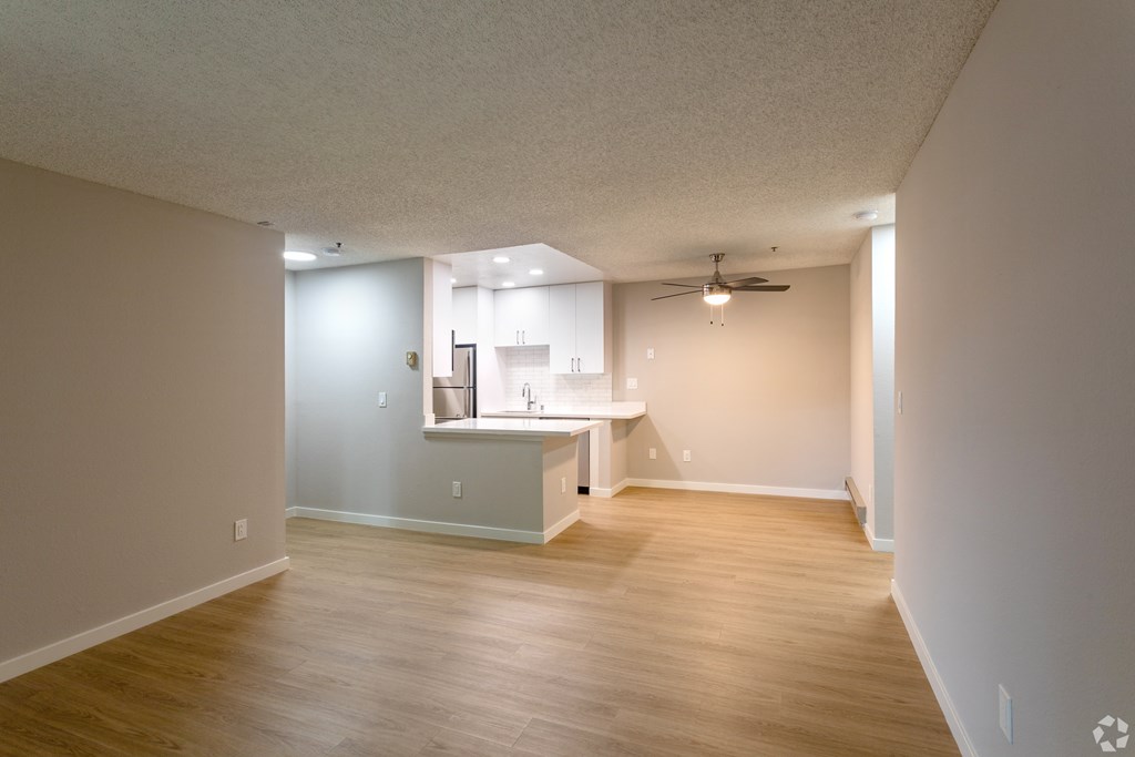 an empty living room and kitchen with wood flooring and a ceiling fan