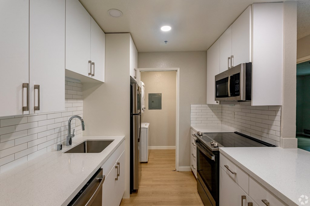 an empty kitchen with white counters and a sink and a refrigerator