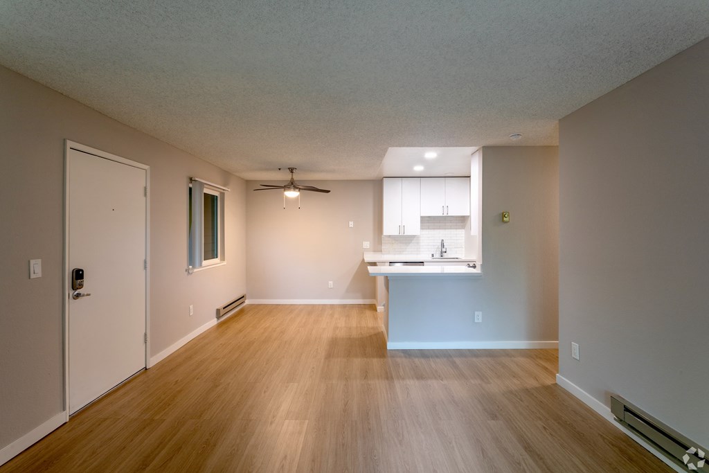 an empty living room and kitchen with wood floors and a ceiling fan