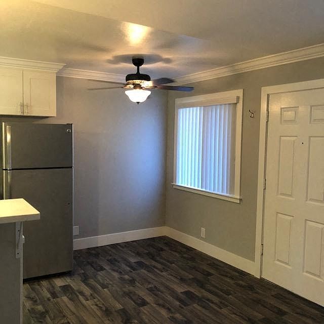 A kitchen with a refrigerator, ceiling fan, and wooden flooring.