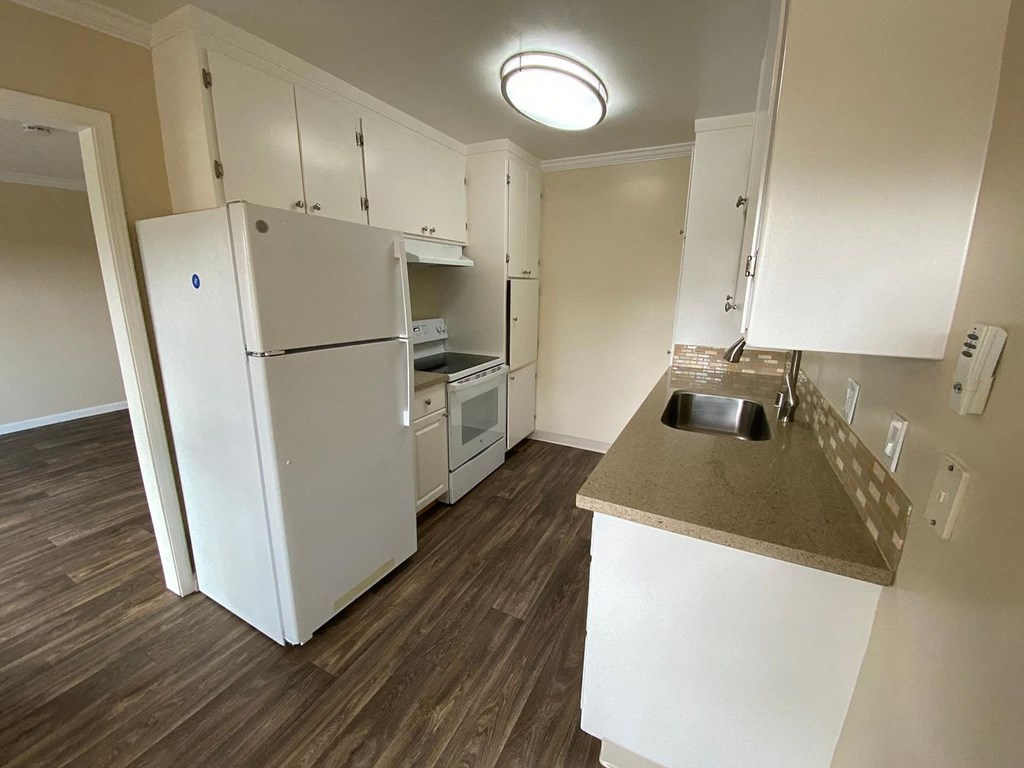 A kitchen with a white refrigerator, sink, and cabinets.