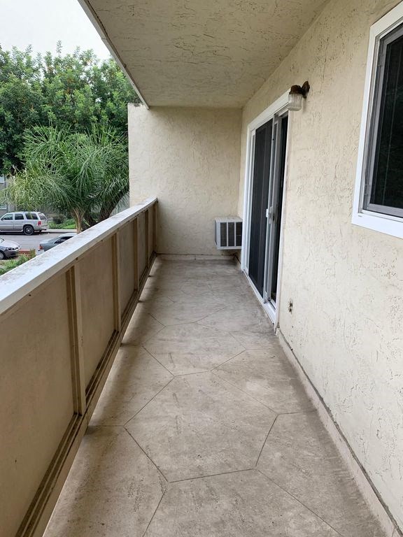 A patio with a tiled floor and a wall with a window and an air conditioning unit.