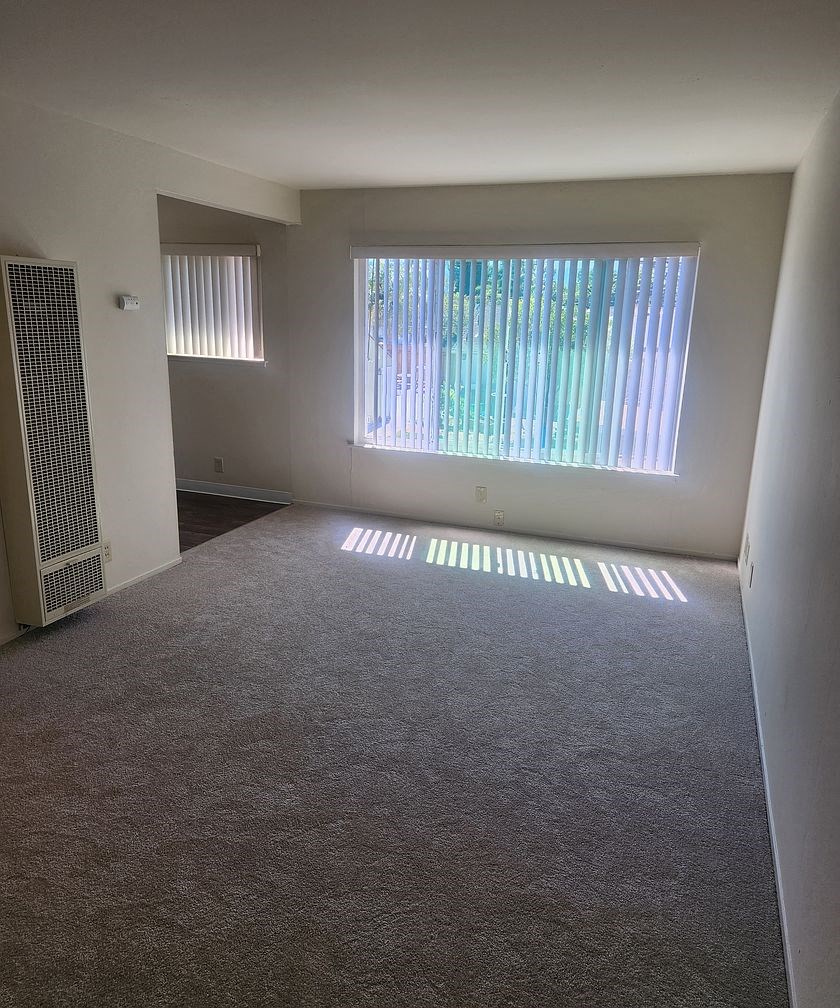 A room with a carpeted floor and a window with blinds.