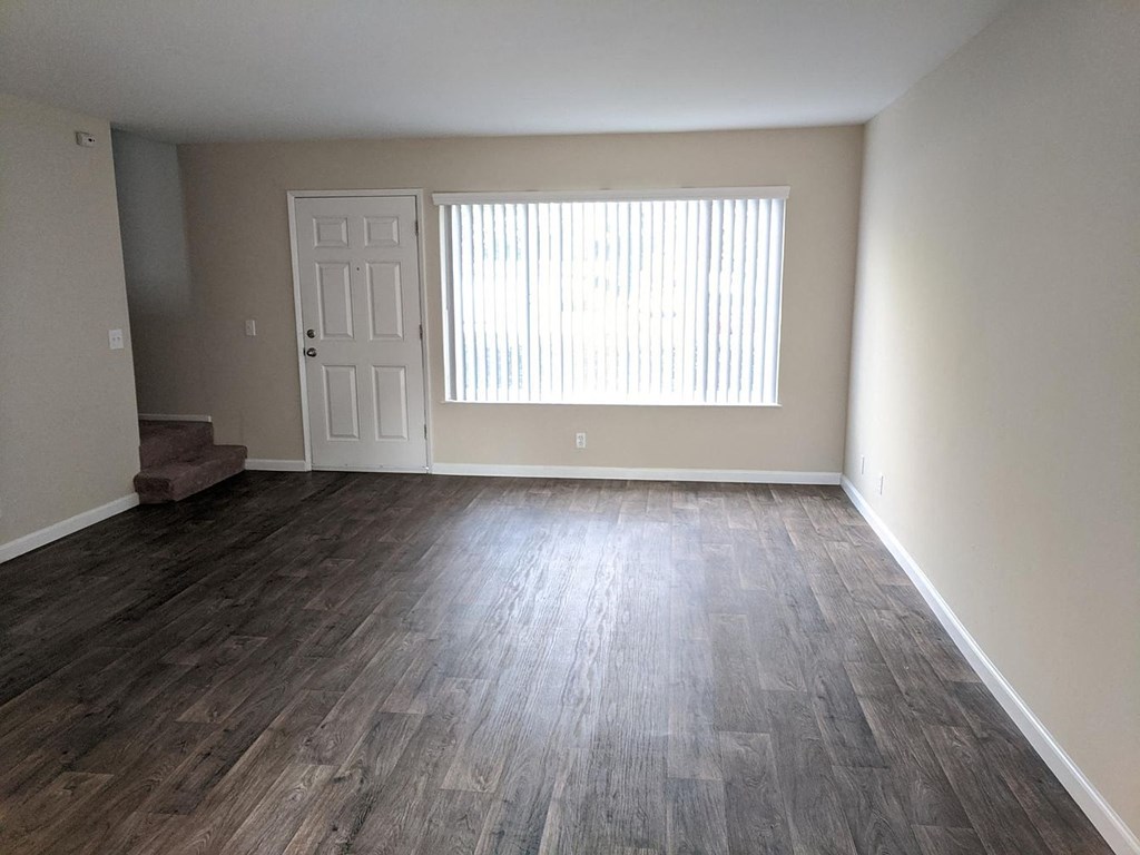 an empty living room with wood flooring and a window