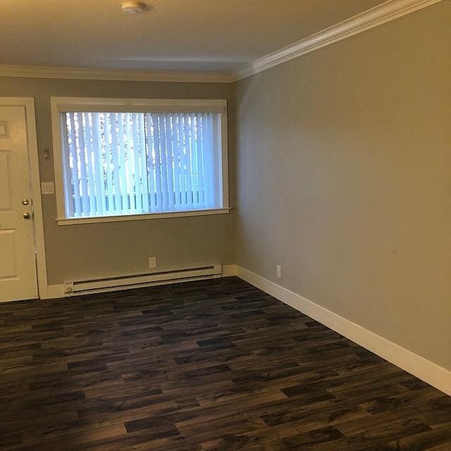 A room with a window covered by white blinds and wooden flooring.