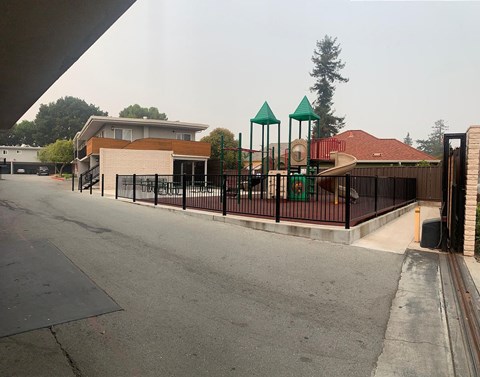 A playground with a green roof and a white building in the background.