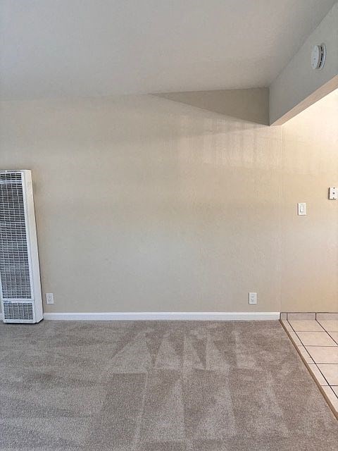 A room with a carpet floor and a wall-mounted air conditioner unit.