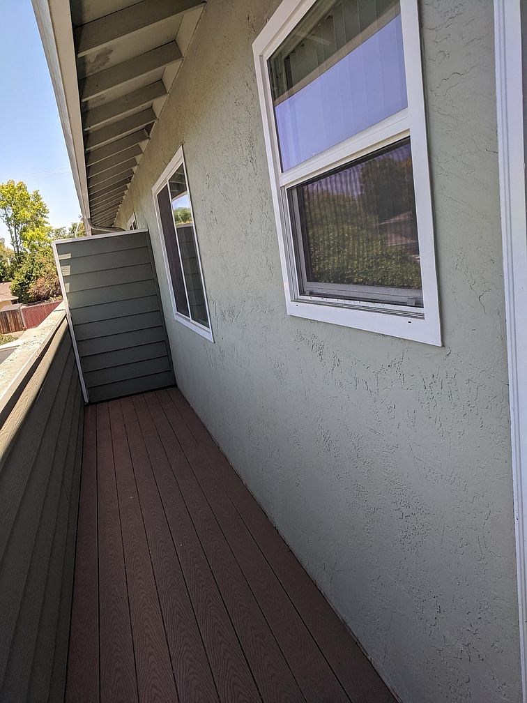 A wooden deck with a white window and a grey wall.