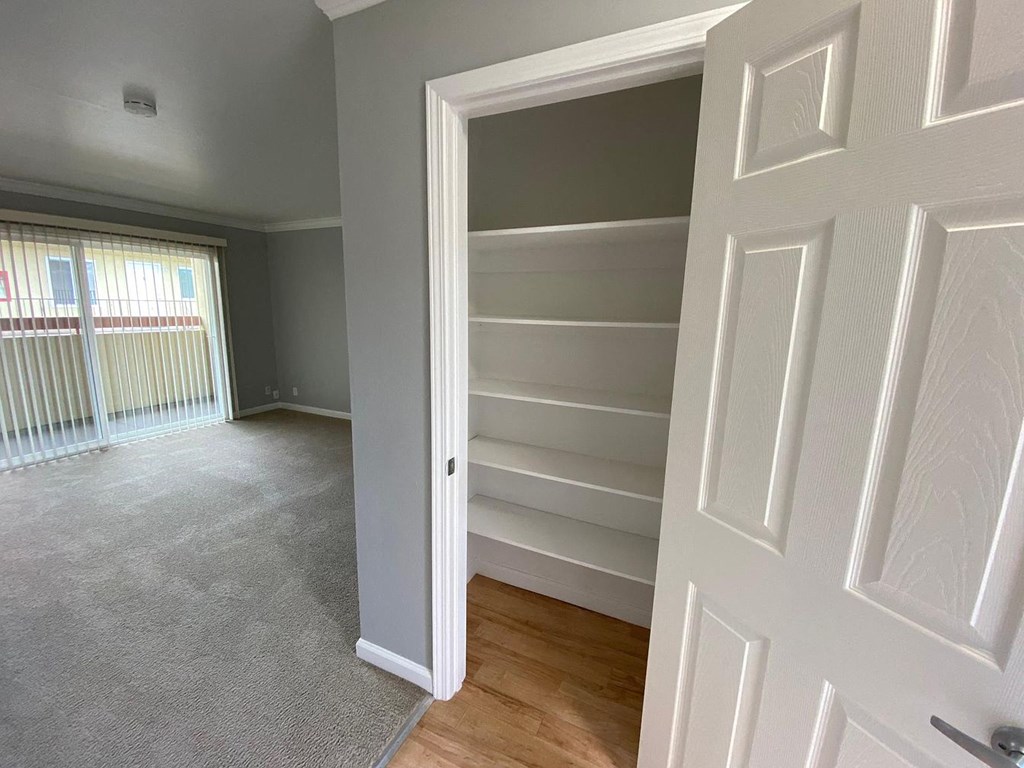 A white door is open to a room with a carpeted floor and a window with blinds.