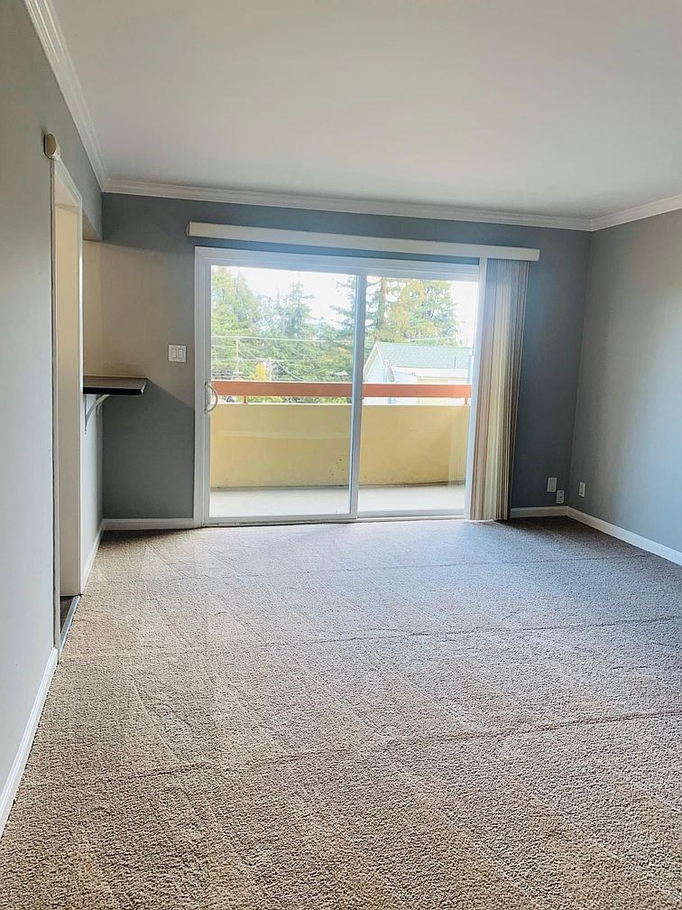 A room with a carpeted floor and a sliding glass door leading to a balcony.