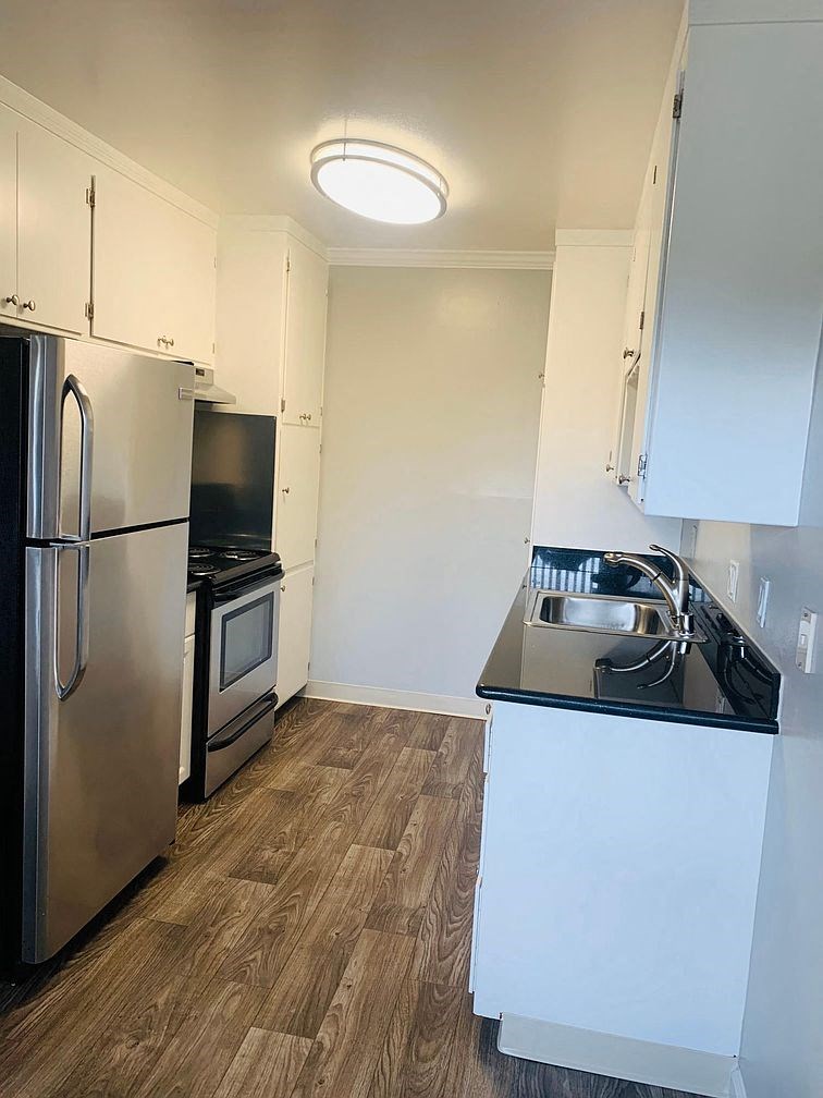 A kitchen with a stainless steel refrigerator and wooden flooring.