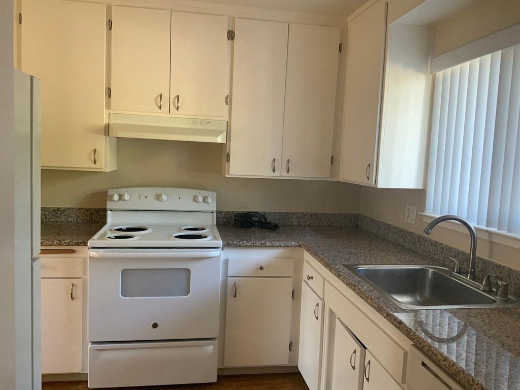A white stove is in a kitchen with white cabinets.