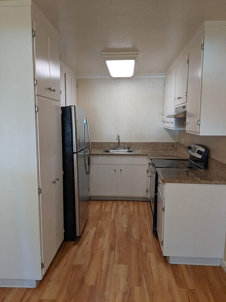A kitchen with white cabinets and a black fridge.