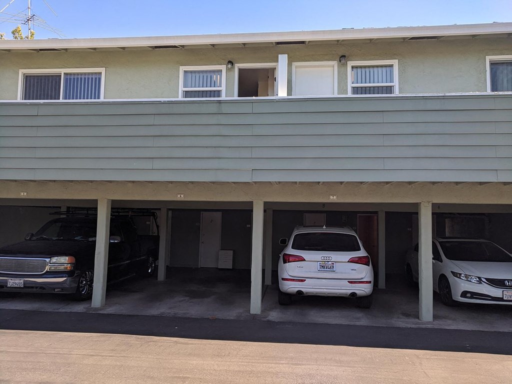 A car is parked in a garage under a house with a window above it.