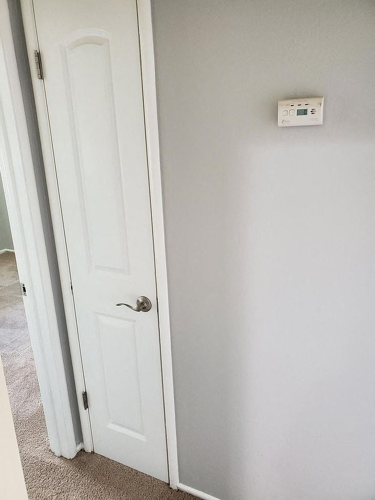 A white door with a white wall and a thermostat on the wall.