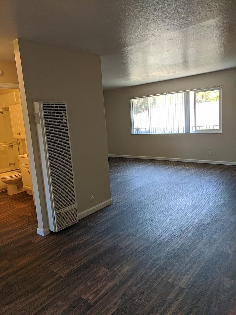 A room with a wood floor and a window with blinds.